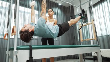 Eğitmen rehberliğinde Pilates Cadillac 'ta ters bacak yükseltme pratiği yapan sağlıklı bir müşteri. Çekirdek dayanıklılığını ve üst vücut dengesini arttırmak için Cadillac 'ı geren adam. Alışkanlık.