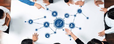 Çeşitli bir ekip, iş stratejileri, veri analizleri ve etkin takım çalışması için proje yönetimi kavramlarını temsil etmek için yenilikçi dijital simgeler kullanarak masa etrafında işbirliği yapar. Dostluk