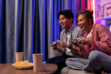 Neşeli, gülümseyen bir çiftin koltuğunda oturup oyun oynuyorlar. Oyun konsolu, hazır aperatifler ve içecekler, modern neon ışıklı, rahat oturma odasında eğlenceli bir rekabet seviyesinde. İnfobahn.