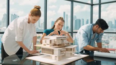 Beyaz proje yöneticisi dizüstü bilgisayar analiz verilerini kullanırken, mimar mühendis ekibi ev modeli inşaatını analiz etmek için birlikte çalışıyor. Bir grup tasarımcı ev tasarımı hakkında konuşuyor. İzleme