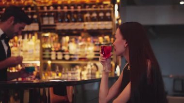 Barmen lüks tezgah barında güzel misafirler için çiçeklerle süslenmiş karışık votka kokteyli servis ediyor. Mükemmel canlı renk sunumu. Atmosfer gece kulübünü ön plana çıkarıyor. Vinosity.