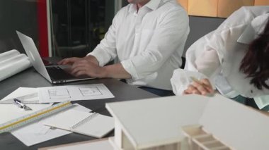 Bir grup mimar mühendis birlikte çalışıyor ve ofis tasarımı hakkında tartışıyorlar. Genç mühendis ev modelini ölçerken yönetici dizüstü bilgisayar kullanıyor. İş tasarımı konsepti. Yönlendirici.