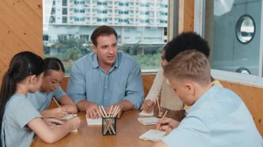 Çok kültürlü çocuklar resim çizerken ya da masa başında kalemle kağıt üzerinde not alırken zeki öğretmen konuşuyor ve işi anlatıyor. Otururken çeşitli öğrenci çizimleri ya da paylaşım fikirleriniz kutlu olsun. Öğretim