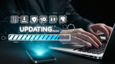 Güncelleme sürecini gösteren dijital arayüzle dizüstü bilgisayarda yazan bir kişi. Karanlık ortam teknoloji temasını vurguluyor, yenilik ve veri güvenliğine işaret ediyor. Dörtgen