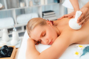 Sıcak bitkisel top spa masaj vücut tedavisi, masör kadın vücuduna nazikçe şifalı bitki torbası bastırıyor. Aromaterapi dinlenme sükuneti ve sükuneti kaplıca salonundaki atmosferi aydınlatıyor. Sessiz.