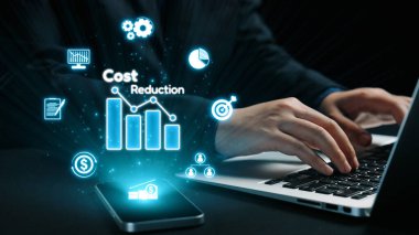 Dizüstü bilgisayar kullanan, dijital grafikler ve maliyet azaltma stratejileri sergileyen, iş analitiği ve verimliliğindeki yenilikleri vurgulayan profesyonel bir çalışma alanı. Dörtgen