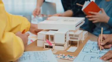 Dinamik mimari atölyesi sahnesinde tartışmalara, çizimlere ve modern bir çalışma alanında bir yapı modeline yer veren bir takım yer alıyor. SACTR