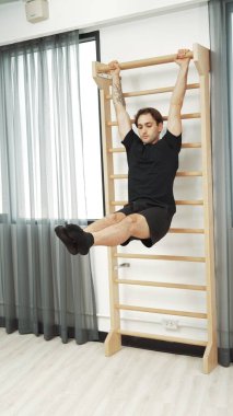 Asılı bacak egzersizi yapan mutlu bir adam vücut kaslarını güçlendirmek ve beden eğitimini iyileştirmek için duvar parmaklıkları üzerinde egzersiz yapıyor. Alt karın bölgesini iyileştirmek için erkek antrenör bacak yükseltme ameliyatı. Alışkanlık.