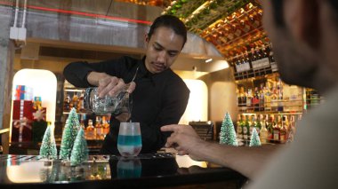 Barmen soğutma bardağına karışık mavi lagün kokteyli dökerken, misafirler içki bekleyen arkadaşlardan bahseder, çam ağacından yapılmış Noel temalı süslemeler özel şenlik tatlandırıcılarını çiftleştirir. Vinosity.