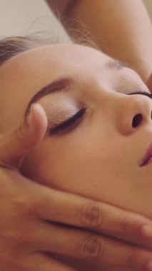 Lüks bir spa merkezinde masaj terapisti tarafından yüz masajı ve spa tedavisi için kaplıcaya uzanmış rahat bir kadın. Sağlık, stres atma ve gençleştirme kavramı.