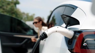Ağır çekimde çalışan kadın şarj aletini şarj istasyonundan elektrikli araba aküsünü şarj etmek için kullandı. Sürdürülebilir çevre dostu seyahat konsepti için alternatif enerji ve şarj edilebilir EV araba. Yararlı