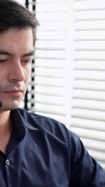 Young competent asian male call center agent working at his computer while simultaneously speaking with customers. Concept of an operator, customer service agent working in the office with headset.