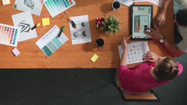 Proje yöneticisi renk paletleri seçerken tasarımcının tablete baktığı yukarıdan aşağıya hava görüntüsü. Profesyonel grafik tasarımının en üst görüntüsü ve logoya bakın. Yetenekli ekip grafikleri seçiyor. Sempozyum.