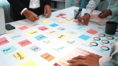 Yaratıcılığı ve verimliliği artırmak için çeşitli notlar, çizelgeler ve dizüstü bilgisayarlar kullanan çeşitli profesyonellerle ortaklaşa beyin fırtınası yapılan canlı bir ofis sahnesi. SACTR