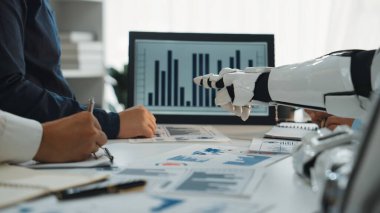 Bir insan ve bir robotu grafik ve grafiklerle veri trendlerini analiz ederken gösteren işbirlikçi bir sahne. Modern çalışma alanı teknolojinin iş analizlerine entegrasyonunu vurgular. Noogenesis