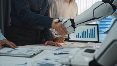 İnsan ve robot kol arasındaki çarpıcı bir tokalaşma görüntüsü, iş yerindeki yeniliği yansıtan teknoloji ve iş evrimindeki artan işbirliğini sembolize eder. Noogenesis