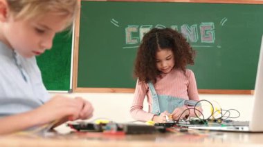 Dizüstü bilgisayar ekranında çalışan çeşitli öğrenci kodlama mühendisliği komut yazılımı ve yapay zeka programlaması yapıyor. Amerikalı kız, erkek makine tamir ederken ekipmanları teftiş ediyor. Pedagoji.
