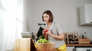 Kafkasyalı anne, modern mutfakta dizüstü bilgisayarda yemek tarifine bakarken salata yapmak için yemek hazırlıyor. Yetenekli ev bekçisi taze sebze kullanarak kahvaltı hazırlıyor. Pedagoji.