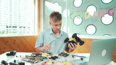 Liseli çocuk, dizüstü bilgisayarlı ve elektrikli aletli araba modelini tamir ediyor. BTMM sınıfında eletronik ekipman kullanırken, gençlerin robot makine inşaatını denetlemesi. Öğretim
