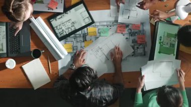 Yöneticinin proje planı yazması ve toplantıda oturması. Bilgisayarlı ve teçhizatlı ev inşaatı hakkında planlar yapan ve paylaşan iş adamlarının havadan görüşü. Sempozyum.