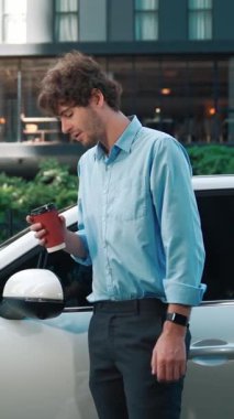 Takım elbiseli, hırslı bir işadamı elektrik kablosu ve yenilenebilir enerji enerjili bir elektrikli araçla şarj istasyonunda dururken elektrikli aracına yaslanıyor..