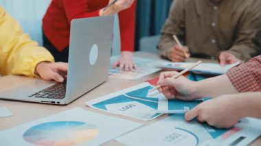 Çeşitli profesyonellerden oluşan bir grup, iş stratejisini geliştirmek için bir dizüstü bilgisayar ve belgelerdeki çizelge ve verileri analiz ederek çağdaş bir ofis ortamında işbirliği yapıyor. SACTR