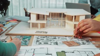 Yaratıcı bir çalışma alanı, ayrıntılı bir mimari model ve planlarla ilgilenen eller sunar. Çevre profesyoneller arasında işbirliği ve tasarım yeniliğini teşvik eder. SACTR