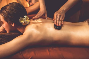 Sıcak mum ışığı olan lüks bir tatil köyündeki kaplıca salonunda sıcak taş masajı yapan mutlu çift, bazalt taşı masajının keyfini çıkarırken rahatlatıcı bir sıcaklıkla vücudun üzerinde süzülüyor. Sessiz.