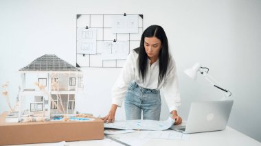 Genç, güzel beyaz bir mimar masanın üzerine plan koyar ve ev modeliyle karşılaştırırken, modern ofisteki fahişe modellerini dikkatlice incelerken arkadaki çizgilerle karşılaştırır. Tertemiz..