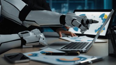 Teknoloji ve otomasyonun veri analizi ve iş dünyasına entegrasyonunu vurgulayan, modern bir ofiste dizüstü bilgisayar ve belgelerle uğraşan gelecekçi bir robot kolu.