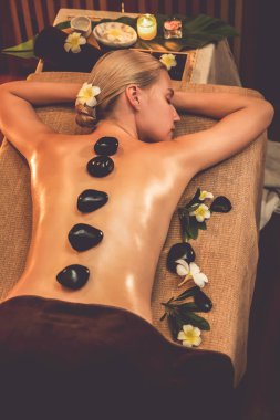 Lüks tatil köyündeki kaplıcalarda sıcak taş masajı, sıcak mum ışığı, spa bazalt taşı masajının keyfini çıkaran mutlu kadın müşteriler, rahatlatıcı bir sıcaklıkla vücudun üzerinde süzülüyorlar. Sessiz.