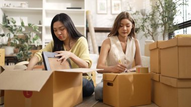 Çekici bir oda arkadaşı oturma odasında paket paketlerken pakette konum yazıyor. Mutlu satıcı birlikte çalışıyor ve teslimat paketini hazırlıyor. Girişimci kargo kutusu paketliyor. Myrmidon.