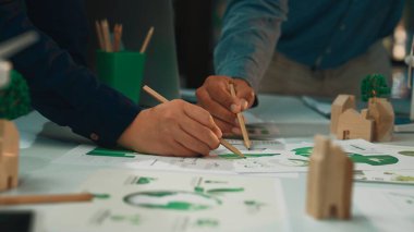 İki birey, yaratıcılık ve yenilikleri ifade etmek için kalem ve sürdürülebilir materyaller kullanarak modern bir çalışma alanında çevre dostu tasarım çizimleri üzerinde işbirliği yapmaktadır. SACTR