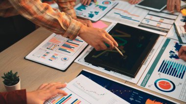 Bir iş ekibi, bir çalışma masası üzerinde çeşitli finansal raporlar, çizelgeler ve grafikler üzerinde işbirliği yaparak, kurumsal stratejide veri analizinin önemini vurgular. SACTR