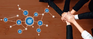 Çeşitli bir ekip, iş ortamlarında hedefe yönelik stratejiler tasvir eden görsel unsurlar zeminine karşı birlik ve ortak çabayı sembolize ederek el ele veriyor. Dostluk