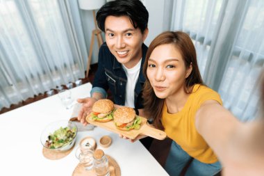 Gülümseyen ev sahibi aşçıların akıllı telefonuyla fotoğraf çekerken üst görüntüsü yemek programında çift hamburger tutarken sosyal medya kanalında ev yapımı salata tabağıyla kolaylıkla görülebiliyor. İnfobahn.