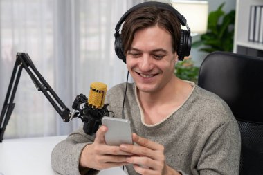 Akıllı yayıncının sunucu kanalı canlı sosyal medya yayını ile akıllı telefon kullanarak dinleyiciyle sohbet ediyor, kulaklık takarak modern ev stüdyosunda video kaydediyor. Bireysel.