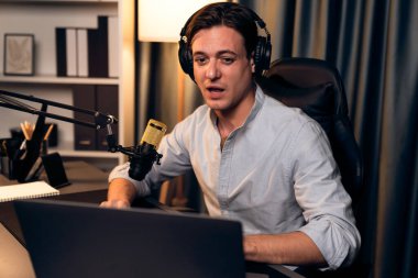 Sunucu kanalı akıllı yayıncı laptopta canlı sosyal medya uygulaması arıyor, kulaklık takıyor ve modern ofis stüdyosundaki mikrofonu kullanıyor. Bireysel.