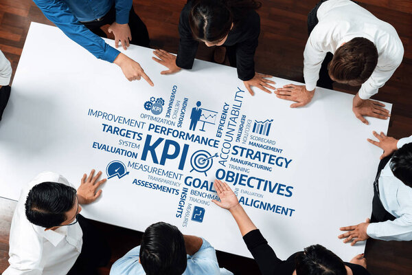 Динамичная команда участвует в совместной стратегической сессии, указывая на ключевые показатели эффективности и цели, представленные на большом листе, способствуя инновациям и совместной работе. Ах!