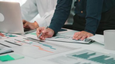 Takım çalışması yapan, stratejileri tartışan ve raporları ve çizelgeleri analiz eden iş adamlarının yer aldığı modern bir ofis sahnesi. İşbirlikçi bir atmosfer. SACTR