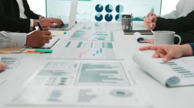 Çeşitli profesyonellerden oluşan bir grup, rapor ve çizelgelerde gösterilen mali verileri analiz ederek, takım çalışması ve stratejik planlamayı sergileyerek çağdaş bir ofiste işbirliği yapıyor. SACTR