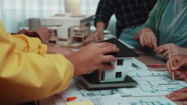 Mimarlar ve müşterilerin ortak bir tasarım sürecine girdiği, bina planları, modelleri, planlar ve fikirleri tartışan ellere odaklanmış dinamik bir sahne. SACTR