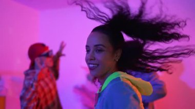Çekici break dansçı, stüdyo arkasında neon ışıkla dans ederken kameraya bakıyor. Profesyonel sanatçı, serbest stile ve hip hop müziğine geçiş yaparken gündelik giysiler giyiyor. Mutluluk.