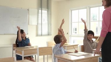 Çeşitli zeki öğrenciler sınıfta çalışırken ve mutlu öğretmenleri dinlerken soruları cevaplamak için ellerini kaldırdılar. Çok kültürlü çocuklar gönüllü oldular, oy verdiler, soru sordular. Pedagoji.