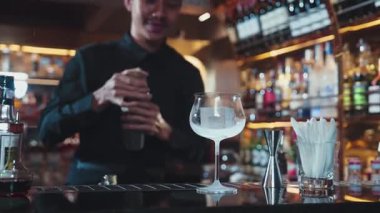 Asyalı akıllı barmen karışık kokteyl sallayarak lüks tezgah hazırlıklarına hazırlanıyor, kameranın önüne bakarak özel bir içecek hazırlıyor. Özel gece hayatı lüksü. Vinosity.