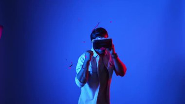 Meta evreni bağlamak için VR gözlük takarken yetenekli oyuncu boksörleri ve yüzen kutuları yumrukluyor. Erkek model, egzersiz yaparken ve neon arka planda dururken sanal gerçeklik gözlüğü kullanıyor. Aygıt.