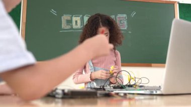Kız tornavida kullanarak elektronik tahtayı tamir ederken ayakta duruyor. Amerikalı öğrenci ve beyaz çocuk elektrik sistemini denetlemek için birlikte çalışıyorlar. Gemide çalışan meraklı çocuklar. Pedagoji.