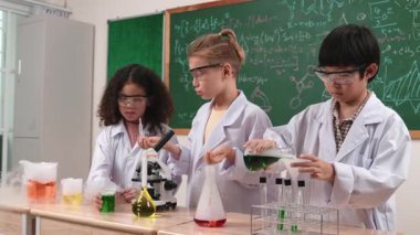 Çocuklar laboratuvarda karatahta başında dururken fen dersinde deney yapıyorlar. Mutlu öğrenci biyokimyasal sıvıyı keşfederken ve incelerken ve karıştırırken. Pedagoji.