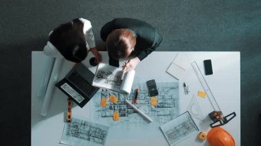 Yetenekli proje yöneticisinin proje planının üst görüntüsü ve toplantı masasında ekipman, cetvel, güvenlik miğferi ve dizüstü bilgisayarı olan mimar mühendise ev tasarımını açıkla. Hizalama.