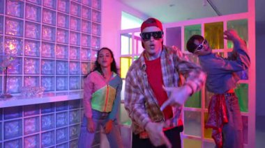 Değişik takımlarla dans ederken süslü gözlük takan yakışıklı hippi serbest stil müzikle mutlulukla dans ediyor. Beyaz hipster kulüpte parlak neon ışıkta sokak dansı yapıyor. Mutluluk.